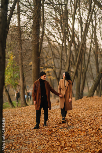 Stylish young couple outdoors on a beautiful autumn day in the forest. Young couple in love holding hands and walking through a park on a autumn day. The concept of youth, love and lifestyle.