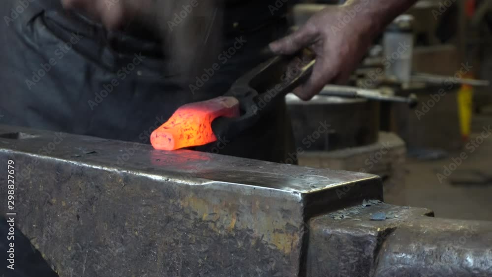 A blacksmith that is working hard to make an object with his hammer. We see the blacksmith make many moves with his hand moving fast. A blacksmith that is working hard to make an object with his hammer. We see the blacksmith make many moves with his hand moving fast.