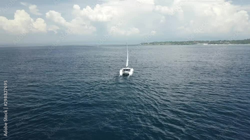 Distant sailboat cruising on a vacation at Nusa Ceningan island Indonesia, aerial shot Distant sailboat cruising on a vacation at Nusa Ceningan island Indonesia, aerial shot