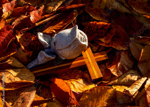 Eine Rose aus Stein mit Holzkreuz zum Abschied im Herbstlaub.