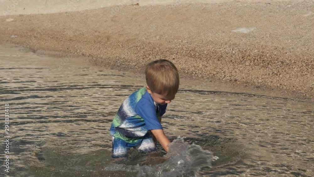 Happy kid boy jumps, playing and splashing in the sea water at summer on a warm sunny day. The child plays on the seashore Happy kid boy jumps, playing and splashing in the sea water at summer on a warm sunny day. The child plays on the seashore