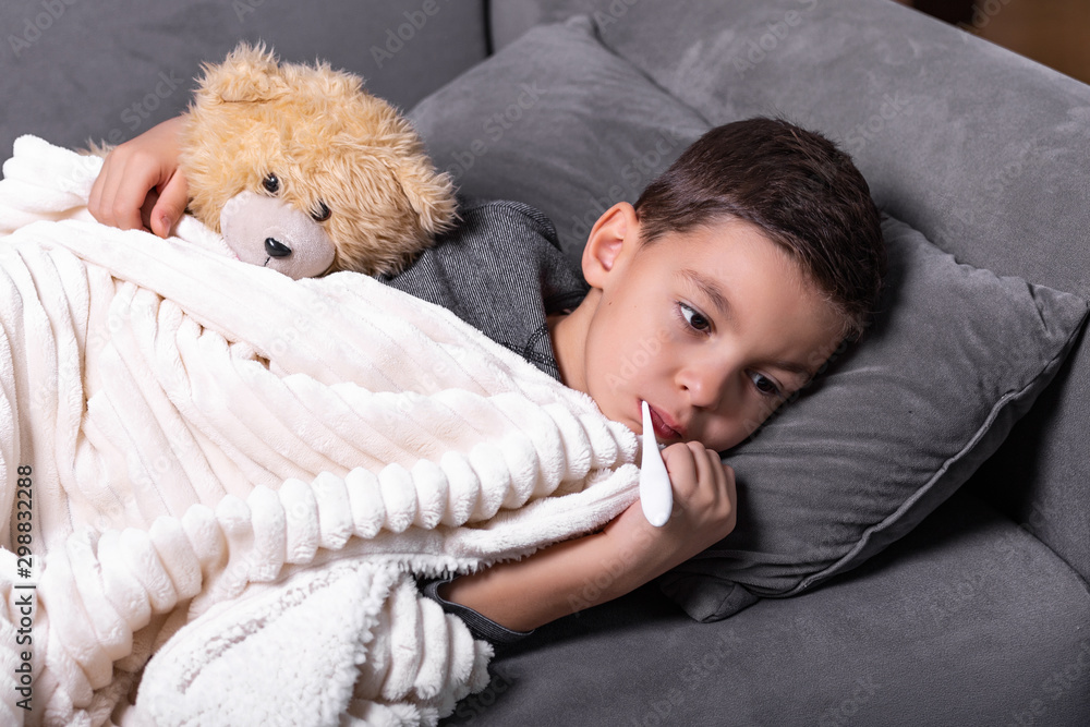 Sick boy with thermometer laying in bed. Sick child with fever and illness in bed. Flu. Cold Sick boy with thermometer laying in bed. Sick child with fever and illness in bed. Flu. Cold