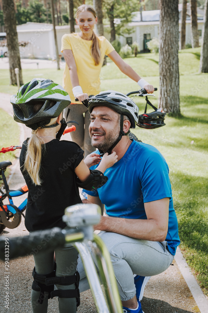 Obraz premium Little girl helping her joyful father to put on bicycle helmet