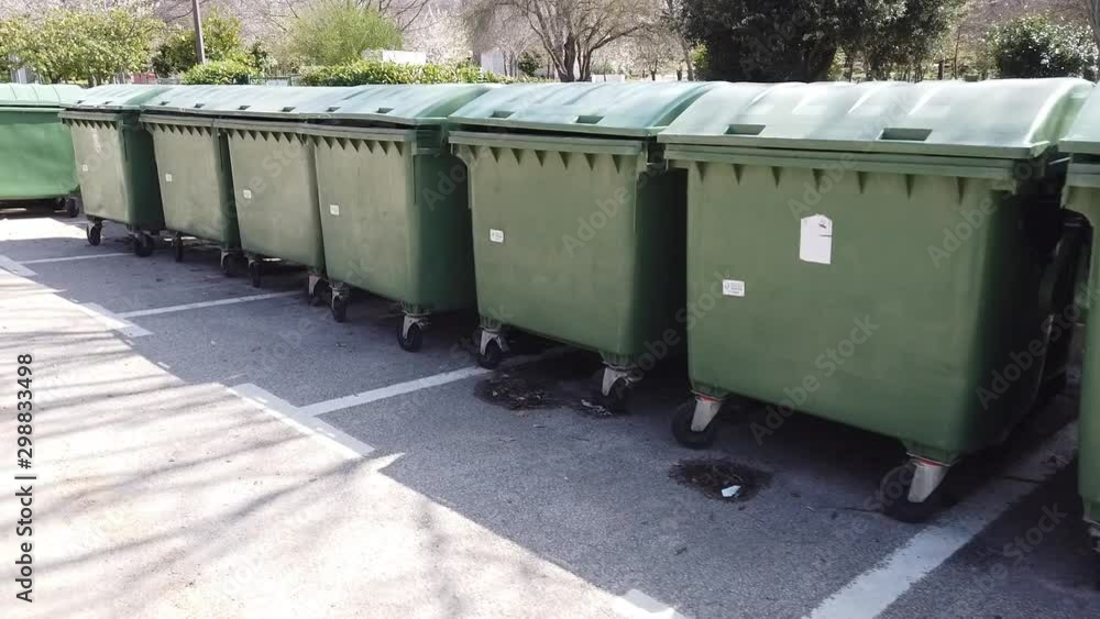 Driving Past Collection Of Large Green Refuse Bins Parked In Car Park Driving Past Collection Of Large Green Refuse Bins Parked In Car Park