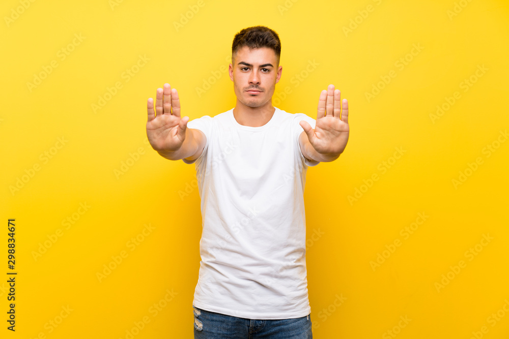 Young handsome man over isolated yellow background making stop gesture and disappointed Young handsome man over isolated yellow background making stop gesture and disappointed