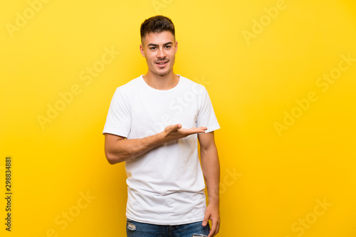Young handsome man over isolated yellow background presenting an idea while looking smiling towards
