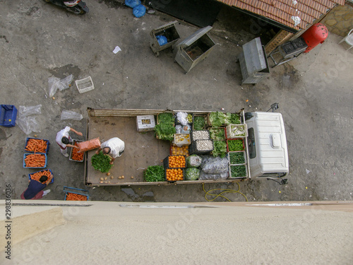 A top view of a truck with crates of vegetables and movers unloading it in the backyard next to dumpsters