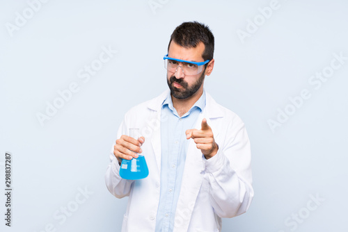 Young scientific holding laboratory flask over isolated background frustrated and pointing to the front