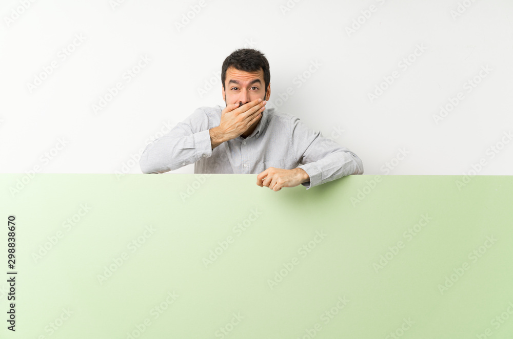 Young handsome man with beard holding a big green empty placard covering mouth with hands Young handsome man with beard holding a big green empty placard covering mouth with hands