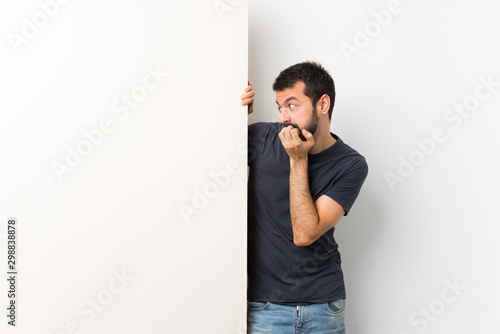 Canvas Print Young handsome man with beard holding a big empty placard nervous and scared put