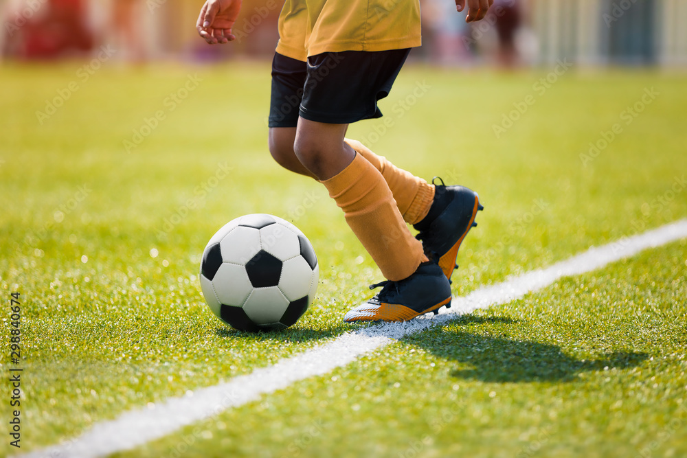 Junior afro american soccer player. Child running with soccer ball along side line of summer grass pitch Junior afro american soccer player. Child running with soccer ball along side line of summer grass pitch