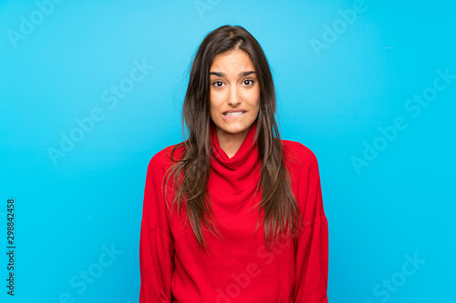 Young woman with red sweater over isolated blue background having doubts and with confuse face expression
