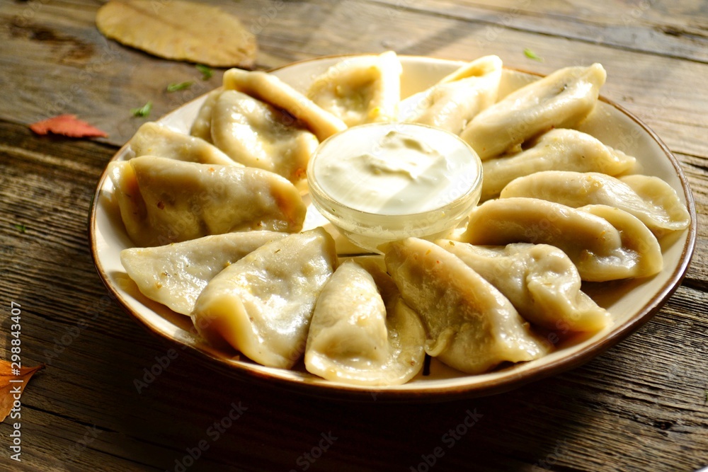 Dumplings in a beautiful plate. Dumplings on a wooden background. Wooden table background with autumn leaves. Appetizing little pie with filling. Traditional homemade food. Dumplings in a beautiful plate. Dumplings on a wooden background. Wooden table background with autumn leaves. Appetizing little pie with filling. Traditional homemade food.