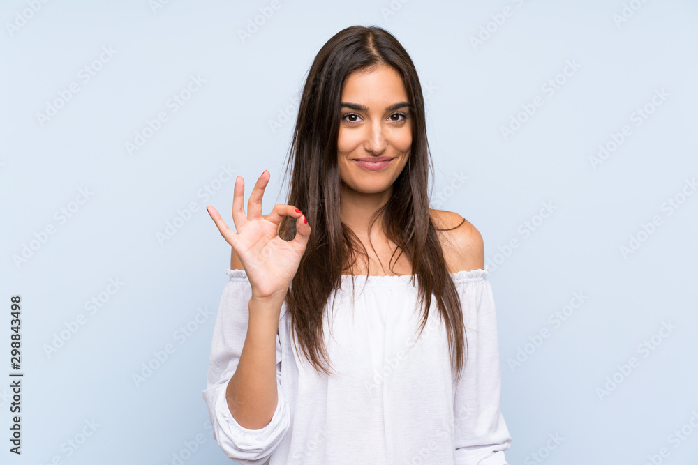 Young woman over isolated blue background showing an ok sign with fingers Young woman over isolated blue background showing an ok sign with fingers