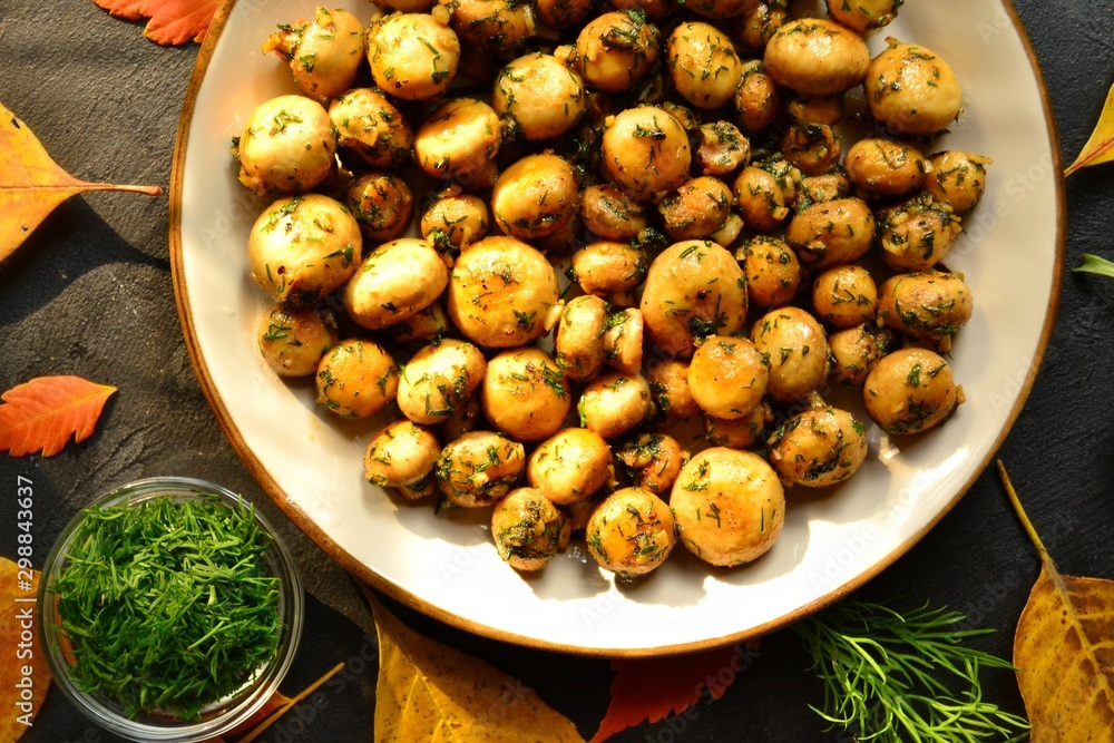 Fototapeta premium Fragrant fried champignons. Grilled mushrooms in a beautiful plate. Autumn leaves. Autumn composition with food, with mushrooms.