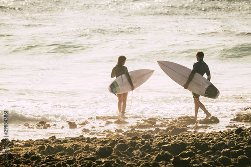 Photography couple of two teenagers or adult entering at the water together to go surfing an