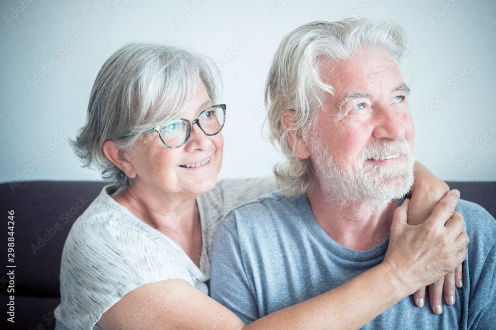 couple of pensioners hugged at home and sitted on the sofa together - two seniors looking at the right couple of pensioners hugged at home and sitted on the sofa together - two seniors looking at the right