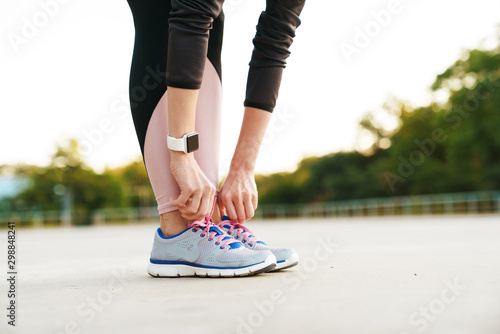 Cropped image of woman wearing tracksuit touching her sneakers outdoors