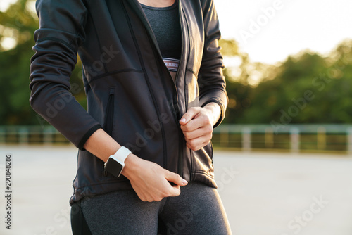 Image of woman wearing tracksuit and wristwatch walking outdoors