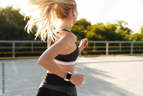 Image of attractive fitness woman wearing tracksuit running outdoors photo