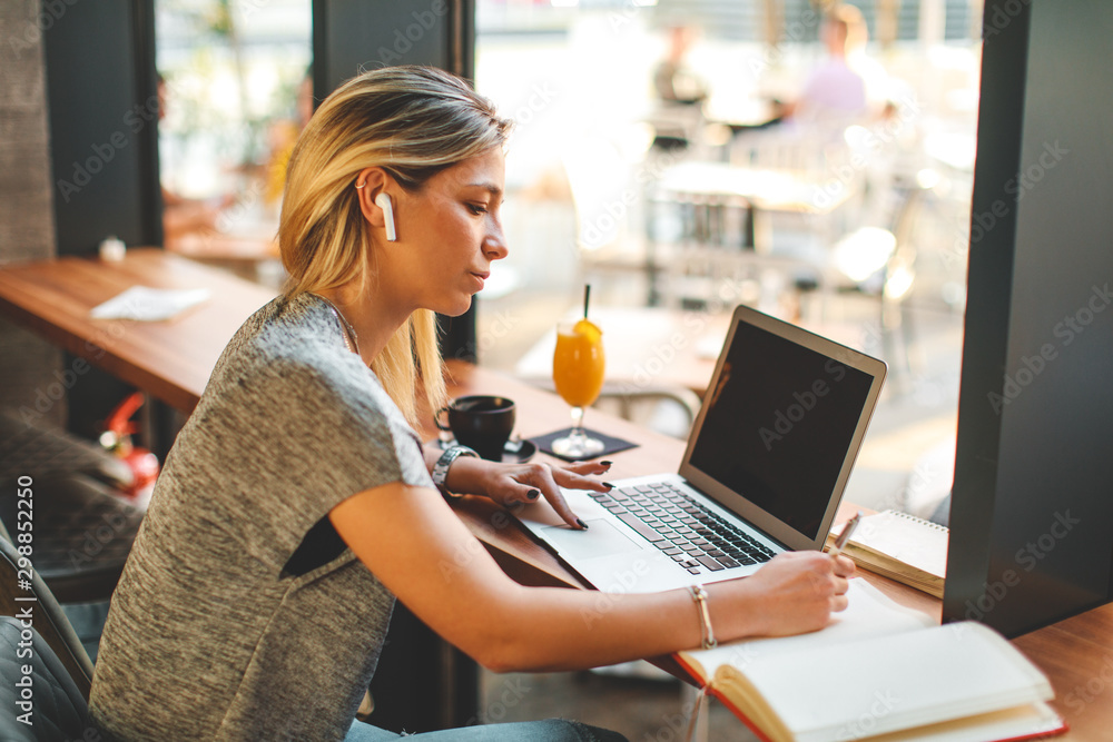 Young woman writing a note with pen with laptop on table at a coffee shop. Young woman writing a note with pen with laptop on table at a coffee shop.