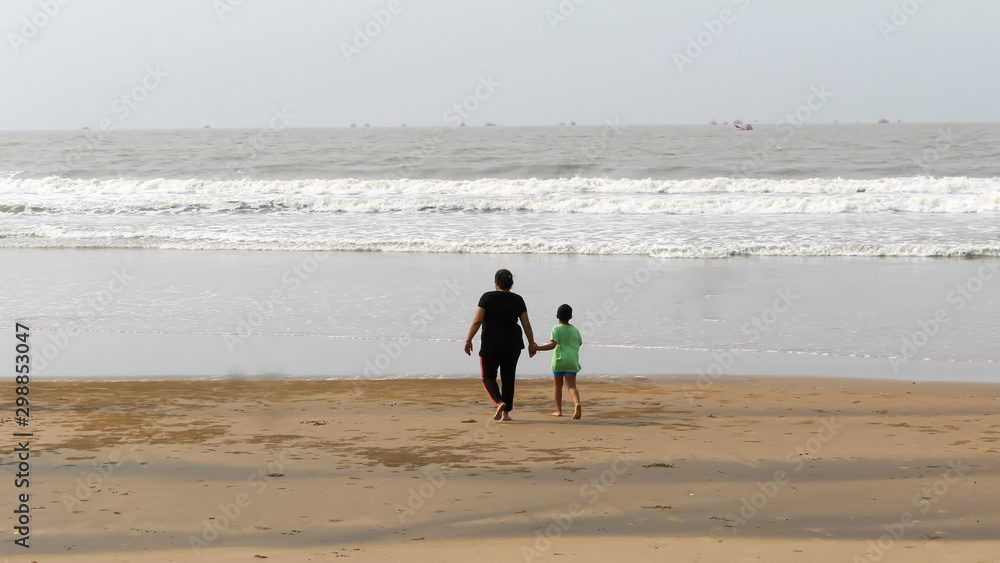 Rear View of Mother and son walking on a tropical beach in evening during sunset. The child admires his mom,s faith. Happy Mother’s day background concept. Goa, India, South Asia Pacific In Summer.