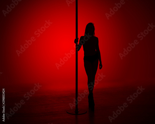 Silhouette of a slender girl while performing dance elements on a pylon. Red gradient background. photo