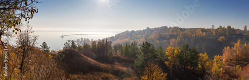 Steep shore of reservoir with trees in morning haze, panoramic