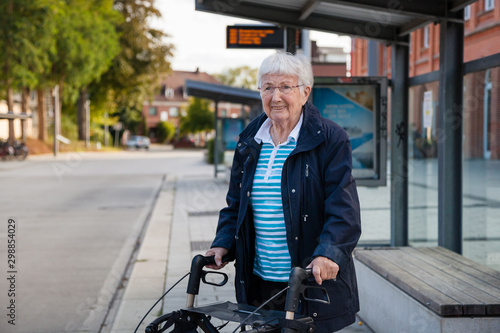 Very old senior woman waiting at the bus stop with walker photo