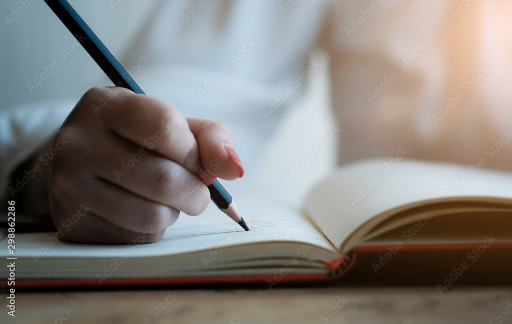 Woman hand with pencil writing on notebook. making notes in notebook with pencil. People writing on notebook and work on wooden table Woman hand with pencil writing on notebook. making notes in notebook with pencil. People writing on notebook and work on wooden table