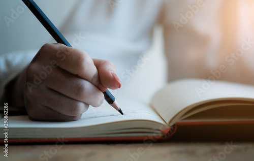 Woman hand with pencil writing on notebook. making notes in notebook with pencil. People writing on notebook and work on wooden table