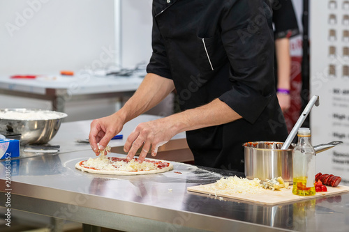 Closeup of a cook in black uniform preparing pizza