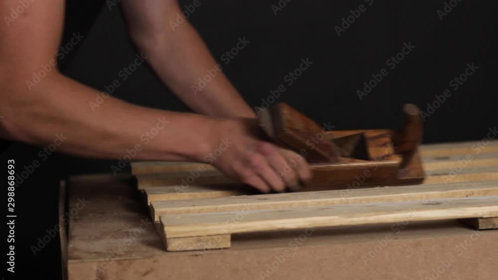 Craftsman shaping wooden planks with a wooden plane tool, closeup handheld Craftsman shaping wooden planks with a wooden plane tool, closeup handheld