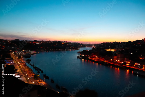 Sunset picture taken from the bridge in Porto, Portugal shows the blue waters f the river and the sky with well lit town on sides