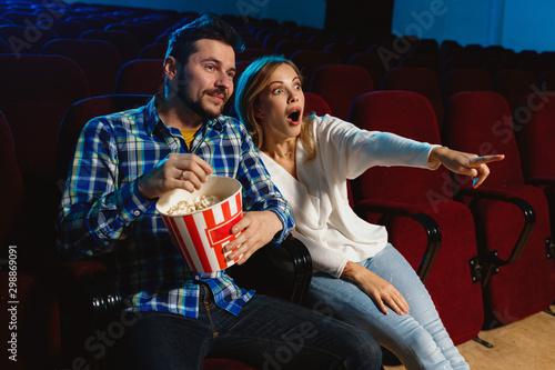 Attractive young caucasian couple watching a film at a movie theater, house or cinema. Look expressive, astonished and emotional. Sitting alone and having fun. Relation, love, family, weekend time.