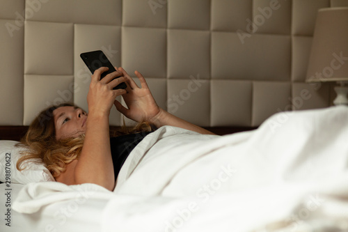 Woman lies in bed with phone, internet addiction. Social network in smartphone.