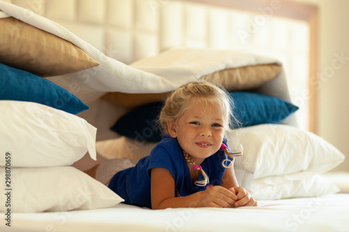 Foto Little cute girl built impromptu fort (castle, house) out of pillows and blankets on bed