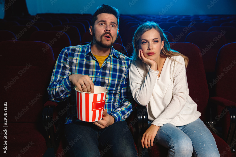 Naklejka premium Attractive young caucasian couple watching a film at a movie theater, house or cinema. Look expressive, astonished and emotional. Sitting alone and having fun. Relation, love, family, weekend time.