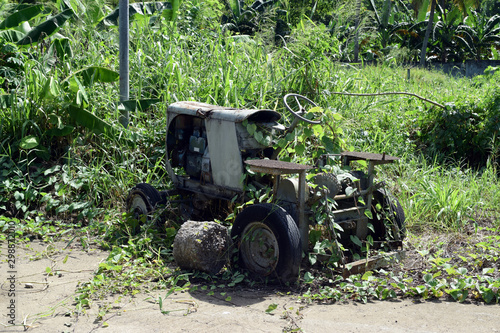 Wasted dilapidated rustic old farm tractor covered by vegetation left on the vicinity of agricultural college campus