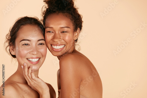 Beauty. Smiling women with perfect face skin and natural makeup portrait. Beautiful happy asian and african girl models with different types of skin on beige background. Spa skin care concept photo