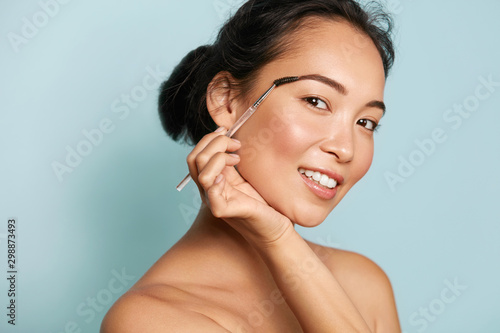 Beauty. Smiling woman brushing eyebrows with makeup brush closeup. Portrait o...