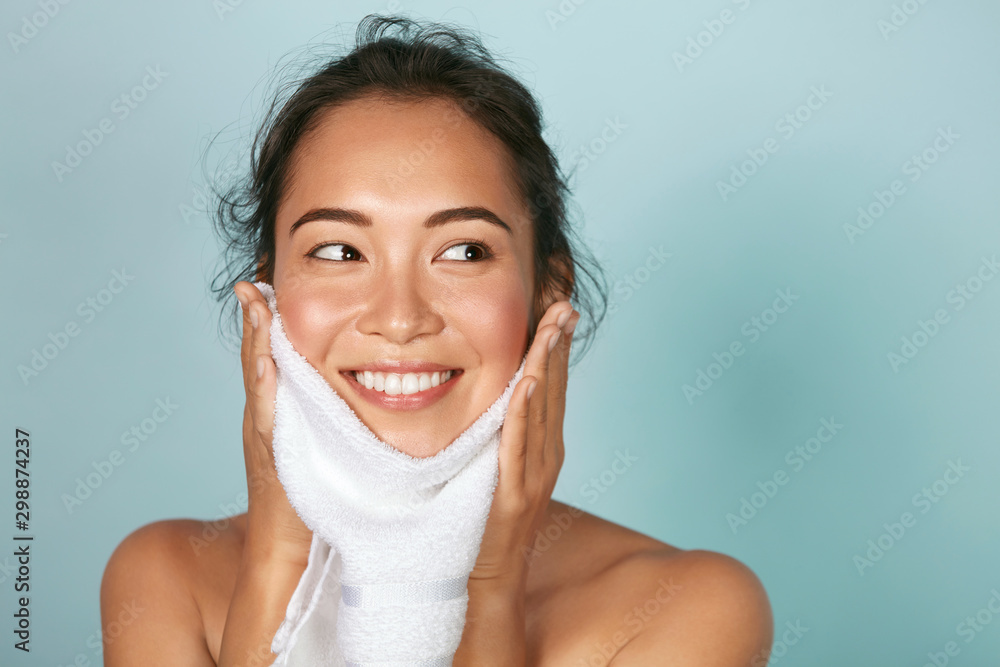 Woman cleaning facial skin with towel after washing face portrait. Beautiful happy smiling young asian female model wiping facial skin with soft towel, removing makeup. High quality studio shot - obrazy, fototapety, plakaty 