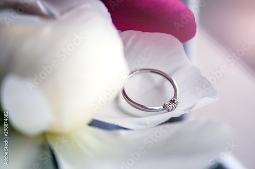 A closeup view of a beautiful white gold engagement ring with three small diamonds in the shape of a heart lying on the petal of white peony