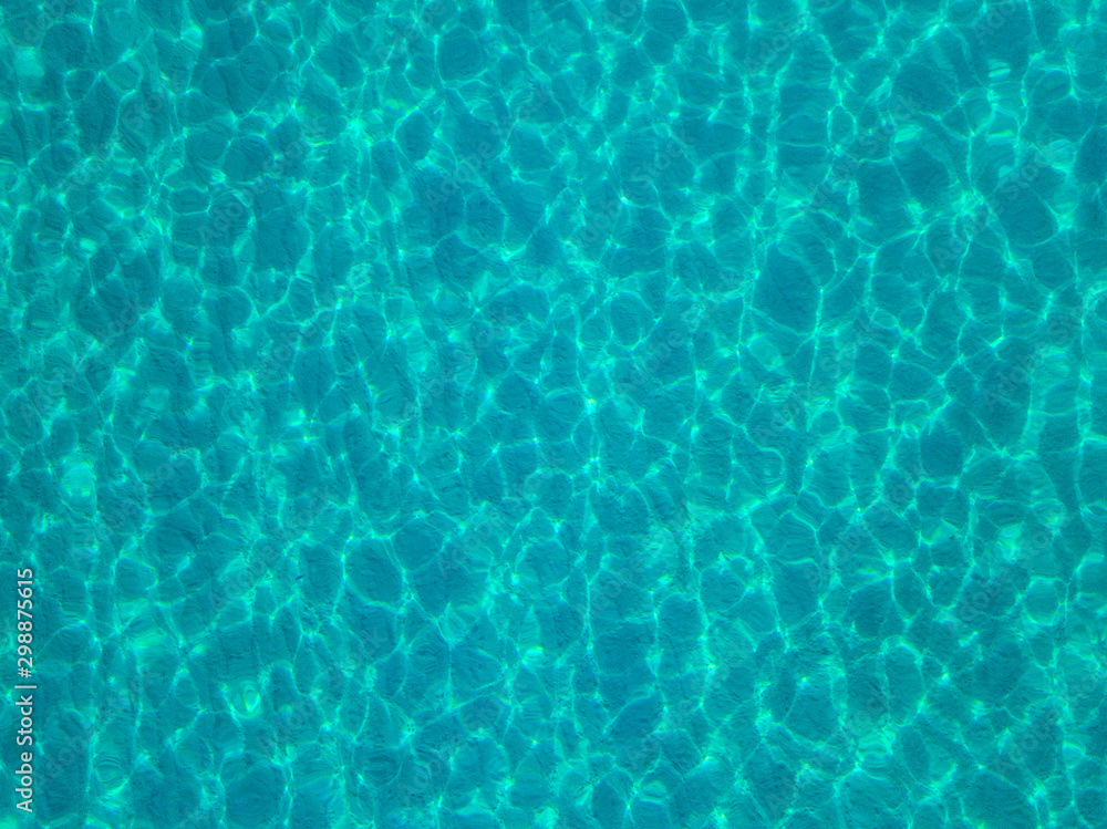 Aerial view of a sandy seabed, crystal clear blue water, reflections of the sun cause ripples on the sea surface. Texture and background. Pool