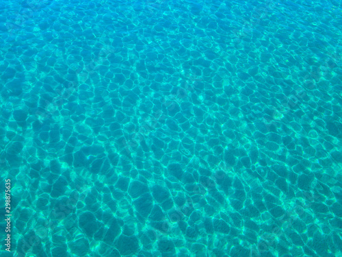 Aerial view of a sandy seabed, crystal clear blue water, reflections of the sun cause ripples on the sea surface. Texture and background. Pool © Naeblys