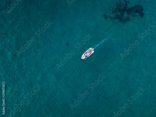 Aerial view of a rowing boat seen from above, powered by an engine. Blue sea that surrounds a boat that crosses it. People inside a boat. 10/22/2019. Pizzo Calabro, Calabria, Italy