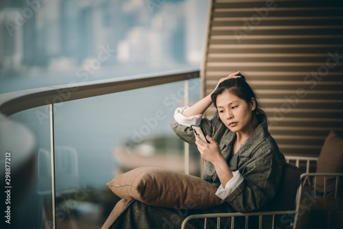 Woman sitting on hotel's balcony and using her smartphone 