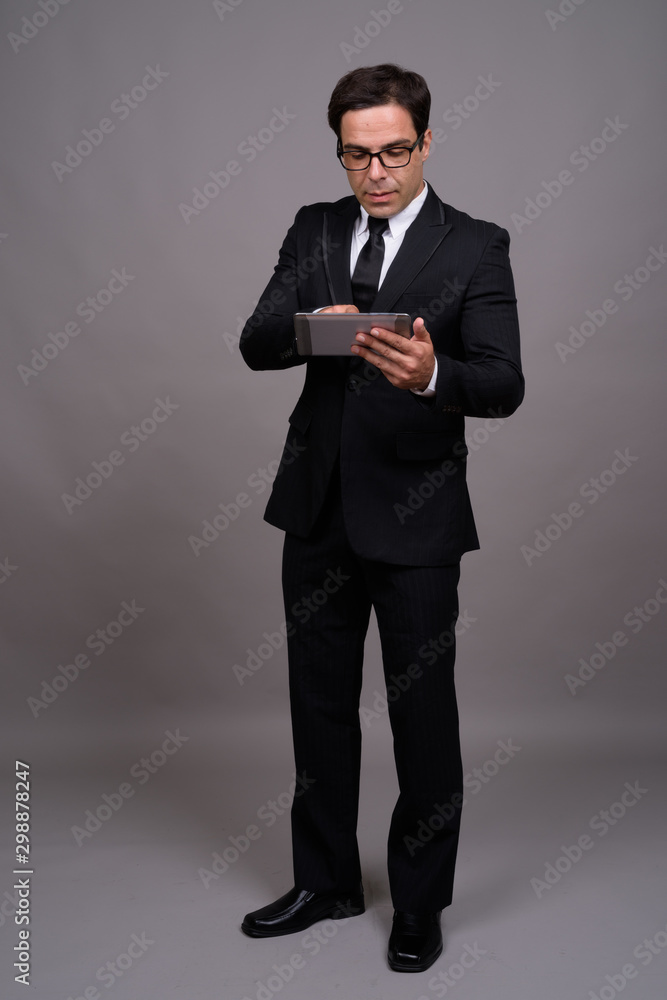Full body shot of Persian businessman in suit using digital tablet Full body shot of Persian businessman in suit using digital tablet