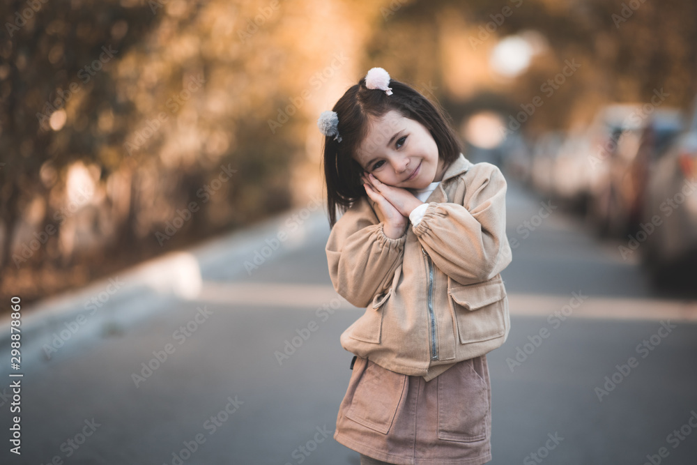 Pretty child girl 3-4 year old wearing stylish autumn clothes posing in street over city background closeup. Looking at camera. Childhood.