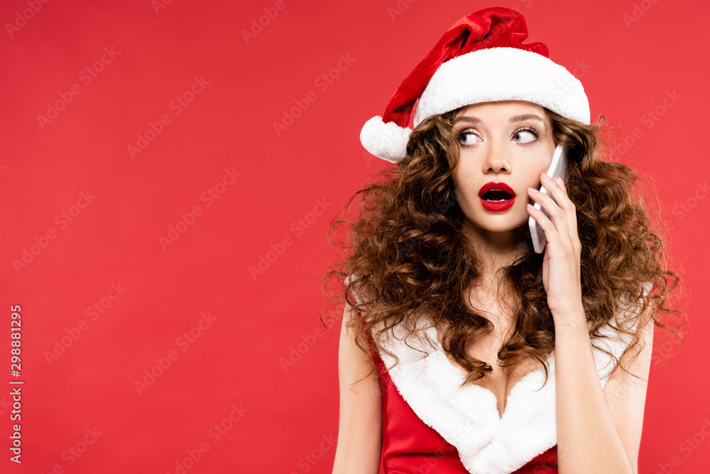 attractive shocked woman in santa costume talking on smartphone, isolated on red attractive shocked woman in santa costume talking on smartphone, isolated on red